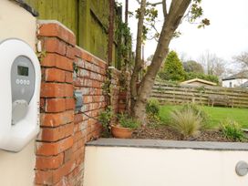 A garden with grass plants a tree a bench and an electric vehicle charging point on a brick wall at Duncombe in Teignmouth