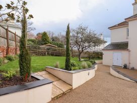 A garden area with grass, trees, a bench, and paved pathways near a house at Duncombe in Teignmouth
