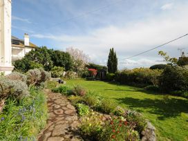 A garden with a stone path flowers grass bushes and trees at Duncombe in Teignmouth