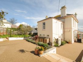 An outdoor area with a beige house a paved patio steps and green plants at Duncombe in Teignmouth