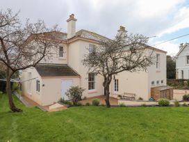 A backyard with grass trees a bench and a cream colored house with chimneys at Duncombe in Teignmouth