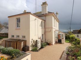 A two-story cream house with pink trim and multiple chimneys surrounded by a gravel driveway and garden at Duncombe in Teignmouth