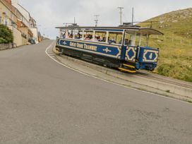 A tram labeled great orme tramway on tracks next to a road with houses and grass hill at Yr Angor (The Anchor) in Llandudno Junction