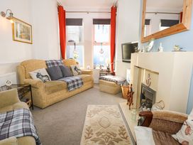 A living room with sofas armchairs a fireplace and windows with red curtains at Yr Angor (The Anchor) in Llandudno Junction