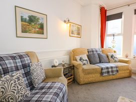 A living room with two sofas, cushions, a side table with decorative plates, wall paintings, and windows with curtains at Yr Angor The Anchor in Llandudno Junction