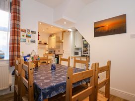 A dining area with a wooden table and chairs and a kitchen in the background at Yr Angor The Anchor in Llandudno Junction