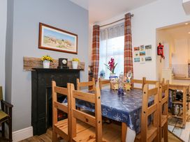 A dining area with wooden chairs around a table covered with a blue tablecloth and a window with plaid curtains at Yr Angor The Anchor in Llandudno Junction
