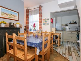 A dining area with wooden chairs and table with a blue tablecloth next to a kitchen with white cabinets at Yr Angor The Anchor in Llandudno Junction