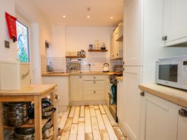 A kitchen with white cabinets a microwave a stove and a wooden shelving unit with pots at Yr Angor (The Anchor) in Llandudno Junction