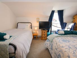 A bedroom with two beds a television on a wooden chest a lamp a chair and blue curtains at Yr Angor The Anchor in Llandudno Junction