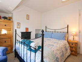 A bedroom with a black metal bed frame blue and white bedding wooden chest of drawers wooden nightstand and small fireplace at Yr Angor The Anchor in Llandudno Junction