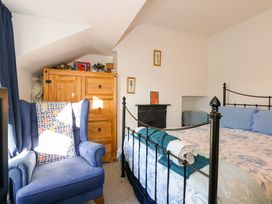 A bedroom with a blue armchair a wooden chest of drawers and a black metal bed frame at Yr Angor The Anchor in Llandudno Junction