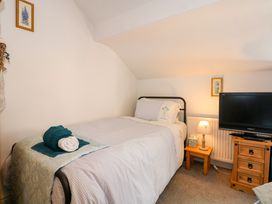 A bedroom with a single bed a bedside table with a lamp and tissue box a wooden chest of drawers and a television at Yr Angor The Anchor in Llandudno Junction