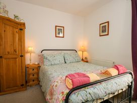 A bedroom with a bed with floral bedding two bedside tables with lamps a wooden wardrobe and framed pictures on the walls at Yr Angor The Anchor in Llandudno Junction