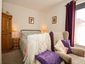 A bedroom with a bed floral bedding armchair with cushions wooden wardrobe and window with purple curtains at Yr Angor The Anchor in Llandudno Junction