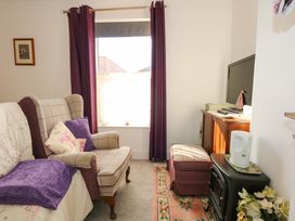 A living room with armchair purple curtains television and electric heater at Yr Angor The Anchor in Llandudno Junction