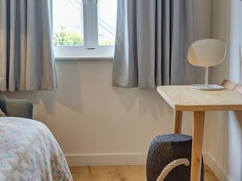 A wooden table with a white mirror on top next to a window with gray curtains and a dark textured stool at Villa 1 in Mullion