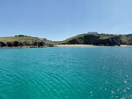 A coastal scene with clear blue water rocky cliffs grassy hills and a sandy beach at Villa 1 Mullion