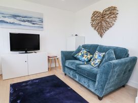 A living room with a blue sofa cushions a television on a white cabinet and wooden heart wall art at Cassia in Kilkhampton