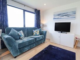 A living room with a blue sofa blue curtains a blue rug a white cabinet with a TV and a wall painting at Cassia in Kilkhampton