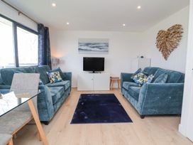 A living room with two blue sofas a black television on a white cabinet and a glass dining table at Cassia in Kilkhampton