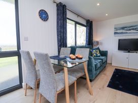 A dining area with a glass table and four grey chairs beside a blue sofa with pillows and a TV on a white cabinet at Cassia in Kilkhampton