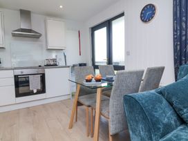 A kitchen and dining area with a glass table and four upholstered chairs next to a blue sofa and a wall clock at Cassia in Kilkhampton