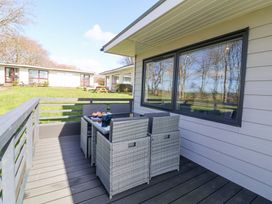 An outdoor deck with a glass table and six wicker chairs next to a house with large windows at Cassia in Kilkhampton