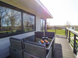 An outdoor deck with a glass table surrounded by four wicker chairs with muffins and cups on the table at Cassia in Kilkhampton