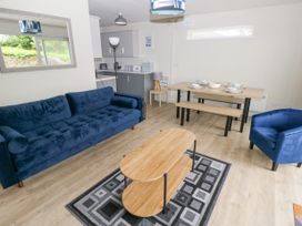 A living room with a blue sofa, blue armchair, wooden coffee table on a patterned rug, and a dining table with benches at 29 Coedrath Park Saundersfoot