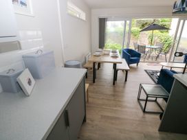 A dining area with a wooden table set for four and blue chairs next to glass sliding doors leading to an outdoor patio with a table and umbrella at 29 Coedrath Park in Saundersfoot