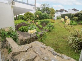 A garden with stone walls grass bushes and flowers near residential houses at 29 Coedrath Park in Saundersfoot