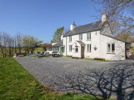 A white two-story house with chimneys a gravel driveway and outdoor seating at Ty'n Pwll Farm in Nefyn