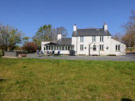 A white two-story house with chimneys a patio with chairs and a table a hot tub and trees on a lawn at Ty'n Pwll Farm in Nefyn
