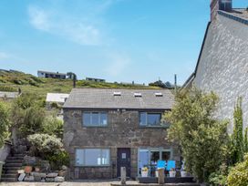 A stone house with multiple windows a dark door and a patio with blue chairs and flower pots at The Cubby Hole in Sennen Cove