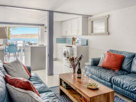 A living room with blue leather sofas, a wooden coffee table, and a kitchen area with white cabinets and a washing machine at The Cubby Hole in Sennen Cove