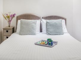 A bed with two pillows a tray with two mugs and a plate with cookies and a bedside table with flowers at The Cubby Hole in Sennen Cove