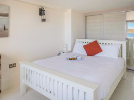 A bedroom with a white wooden bed with white bedding and an orange cushion and a tray with cups and food on the bed with sliding closet doors and a window overlooking water at The Cubby Hole in Sennen Cove