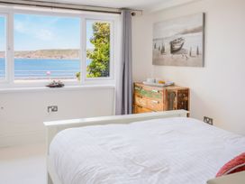 A bedroom with a white bed a distressed wooden dresser and a window showing a sea view at The Cubby Hole in Sennen Cove
