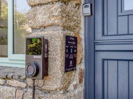 An electric vehicle charging point mounted on a stone wall next to a blue door at The Cubby Hole in Sennen Cove