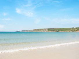 A sandy beach with clear water and a grassy headland in the background at The Cubby Hole in Sennen Cove
