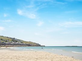 A sandy beach with a few people near the water and houses on a hill at The Cubby Hole in Sennen Cove