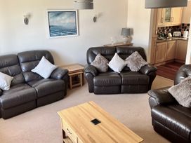 A living room with three brown leather sofas with cushions a wooden coffee table and side tables and a kitchen visible through an open doorway at Penpraze in Portreath