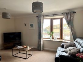 A living room with a black leather sofa a wooden coffee table with a bowl of fruit a television on a stand and a window with curtains at Penpraze in Portreath