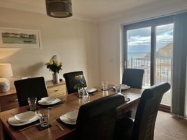 A dining room with a wooden table set for six with black chairs and a view of the sea through glass doors at Penpraze Portreath