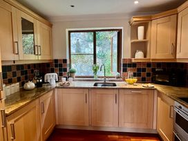 A kitchen with wooden cabinets a sink under a window and a countertop with a toaster a coffee maker cups and a jug with orange juice at Penpraze in Portreath