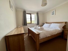 A bedroom with a wooden bed with white bedding two rolled towels on it a wooden dresser and a window with grey curtains at Penpraze in Portreath