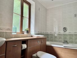 A bathroom with a wooden cabinet under a window next to a bathtub with tiled walls at Penpraze in Portreath