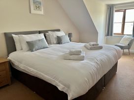 A bedroom with a double bed with white linens and pillows bedside tables a chair near a window and a framed picture on the wall at Penpraze in Portreath