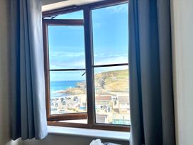 A window with blue curtains showing a coastal view with buildings cars and cliffs at Penpraze in Portreath